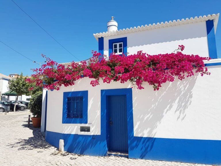 Fachada de casa branca e azul com flores na vila da Ericeira